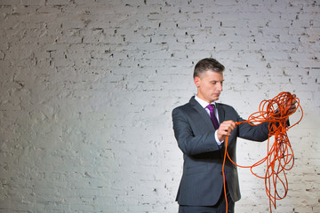 Confident mature businessman holding tangled cable against white brick wall