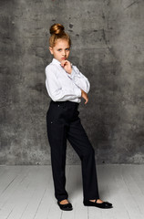Fototapeta premium Little female caucasian model posing in school uniform on a gray concrete studio background.