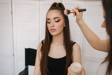 Female makeup master use a powder brush. Beautiful model in beauty studio. Professional make up...