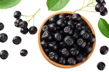 Chokeberry in wooden bowl with green leaves isolated on white background. Black aronia. Top view.