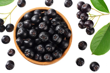 Chokeberry in wooden bowl with green leaves isolated on white background. Black aronia. Top view.