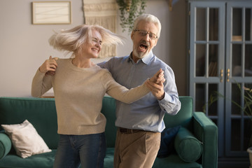 Carefree happy active old couple dancing laughing in living room