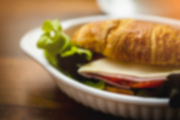 blurred of Ham Cheese Croissant with fresh vegetable in white bowl and hot latte art coffee on wooden table in coffee shop.