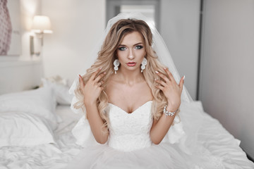 Naklejka premium The bride's fees at the hotel. A beautiful blonde is standing at the window in a wedding dress.