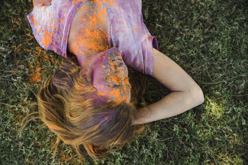 An orange holi color on woman's face lying on green grass