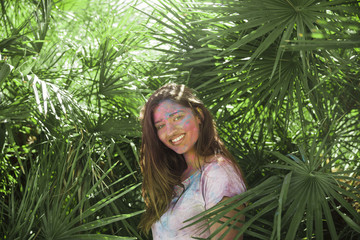 Smiling young woman with holi color on her body standing among the green palm leaves