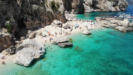 View from above, stunning aerial view of a beautiful beach full of beach umbrellas and people sunbathing and swimming on a turquoise water. Cala Gonone, Sardinia, Italy, Cala Mariolu