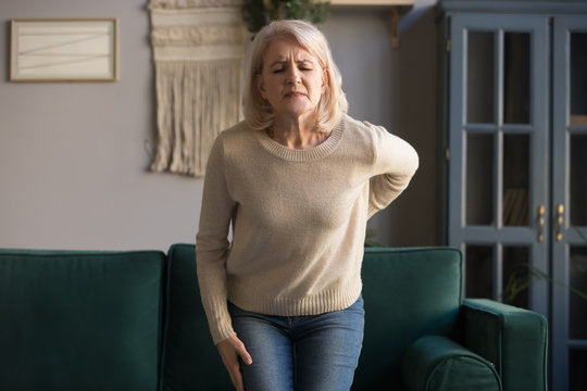 Upset old woman touching sore spine feel sudden back pain