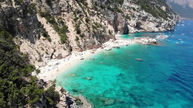 View from above, stunning aerial view of a beautiful beach full of beach umbrellas and people sunbathing and swimming on a turquoise water. Cala Gonone, Sardinia, Italy, Cala Mariolu