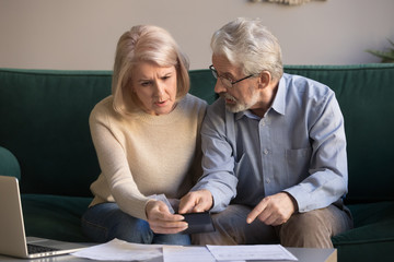 Serious stressed old couple looking at calculator feeling worried