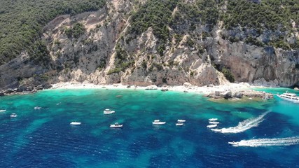 View from above, stunning aerial view of a beautiful beach full of beach umbrellas and people sunbathing and swimming on a turquoise water. Cala Gonone, Sardinia, Italy, Cala Mariolu