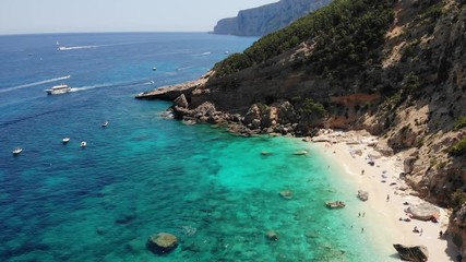 View from above, stunning aerial view of a beautiful beach full of beach umbrellas and people sunbathing and swimming on a turquoise water. Cala Gonone, Sardinia, Italy, Cala Mariolu