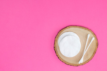 Cotton pads and sticks on round wooden stand, bright pink background. Cosmetology, healthcare, make-up concept. Top view, flat lay, copy space, mock up, layout design.