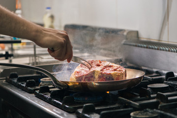 Chef's hands preparing T-bone steak on the grill pan.