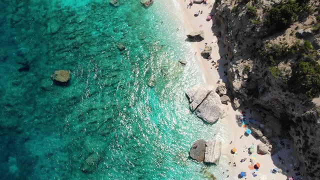 View from above, stunning aerial view of a beautiful beach full of beach umbrellas and people sunbathing and swimming on a turquoise water. Cala Gonone, Sardinia, Italy, Cala Galaritze beach