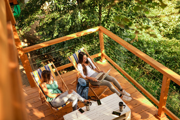 Two female friends relaxing on a wooden balcony in woods.