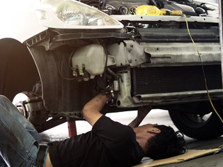 A Man is lying down and working under car at auto service garage. Engine Maintenance concept.Auto car repair service.