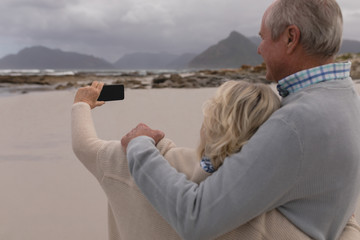 Happy senior couple taking selfie with mobile phone standing at the beach