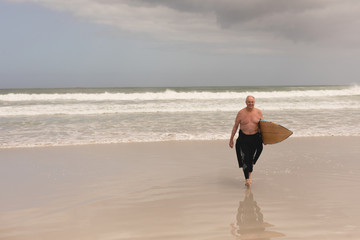 Senior man out of the water with her surfboard on the beach