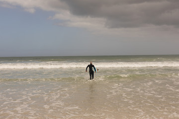 Senior female surfer walking with surfboard on the beach