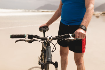 Senior man standing with bicycle on the beach