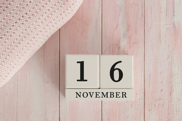 16 November Date on Cubes. Date on painted pink wood, next to baby blanket. Theme of baby due dates and birth dates.