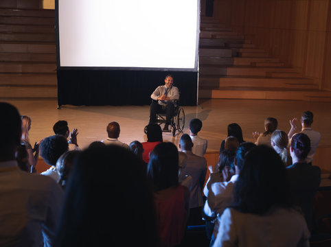 Businessman sitting on a wheelchair and giving presentation to the audience - Powered by Adobe