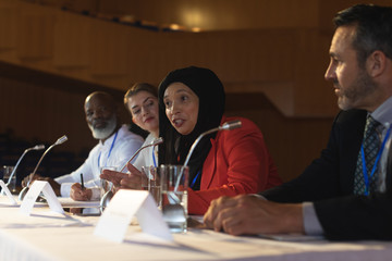 Businesswoman with executive speaking in speaker while sitting in the auditorium