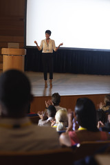 Businesswoman standing and giving presentation in front of the audience in auditorium 