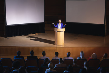 Businesswoman standing around podium and giving presentation to the audience