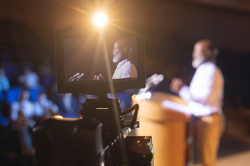 Camera recording businessman giving speech in auditorium 