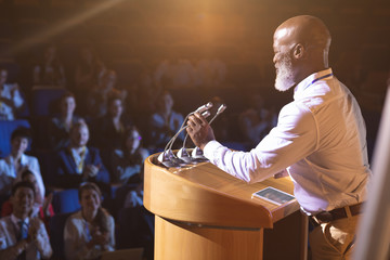 Businessman standing near podium and giving speech to the audience in the auditorium
