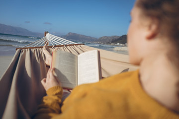 Woman reading book while lying on hammock at beach 