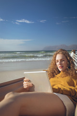 Fototapeta premium Woman using digital tablet while lying on hammock at beach 