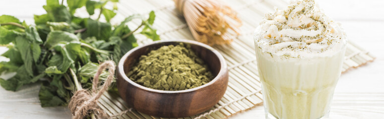 matcha green tea with whipped cream on bamboo mat with powder, mint and whisk