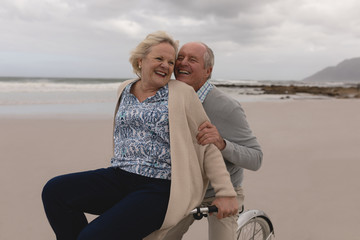 Senior man with senior woman riding bicycle on the beach