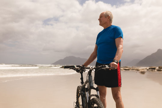 Senior man standing with bicycle on the beach