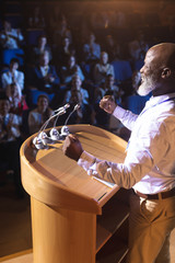 Businessman standing near podium and giving speech to the audience in the auditorium