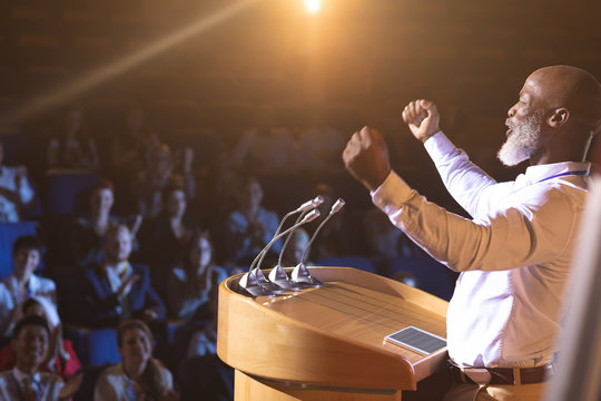 Businessman standing near podium and giving speech to the audience in the auditorium