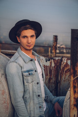 Urban man with hat against the background of the city. Wearing white shirt and jeans. Old neglected...