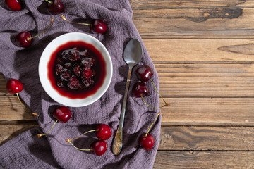 Concept Fresh cherries and plate of jam on old wooden background with vintage cotton napkin as dessert for advertising