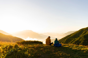 Loving couple sit on the top of the mountain and enjoy the view of the clouds and the sunset. Romantic relationship. A date in the nature. Bzerpinsky cornice of Caucasus. © Ilona