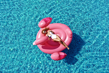 Beautiful  sexy woman inflatable giant pink flamingo float mattress in blue swimming pool with text space. Summer vibes tourist