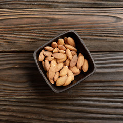 Flat lay view at roasted almond nuts in clay bowl on kitchen wooden table. Copy space
