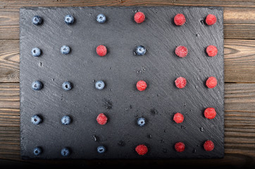 Flat lay view at ripe bilberry and raspberry berries on slate stone tray closeup