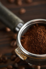 Portafilter filled with fresh ground coffee under dark surface with coffee beans