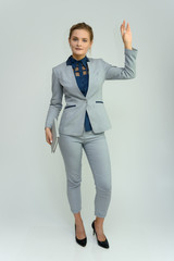 Full length studio portrait of a pretty young woman girl in a business suit on a white background with a folder in hands. He stands right in front of the camera, explains, with emotion.