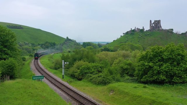 Aerial of an old steam train passes the ruins of Corfe Castle, Dorset, England.