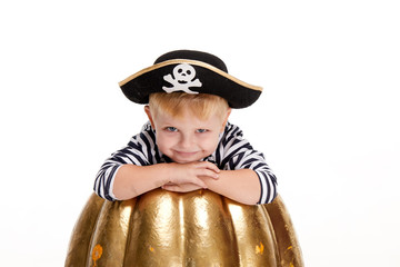 Happy child on Halloween. Funny little boy in carnival costumes of pirates standing with a big pumpkin on white background. trick or treat