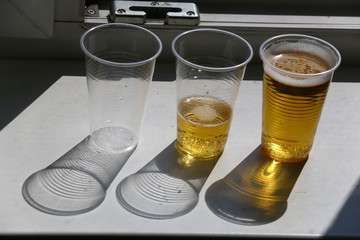 Three plastic cups, one empty and two with beer and a shadow from them on white.